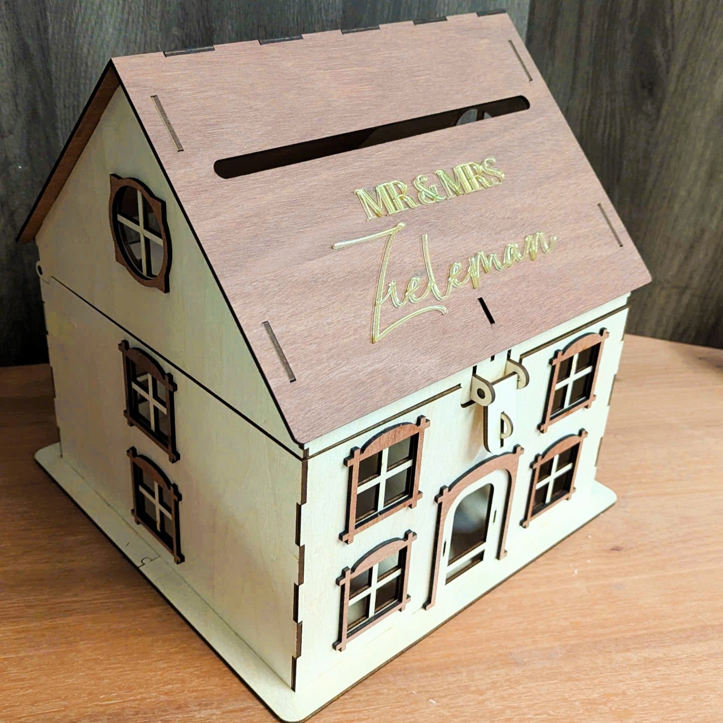 Wooden house-shaped box with 'Mr & Mrs' on the roof, placed on a wooden surface.