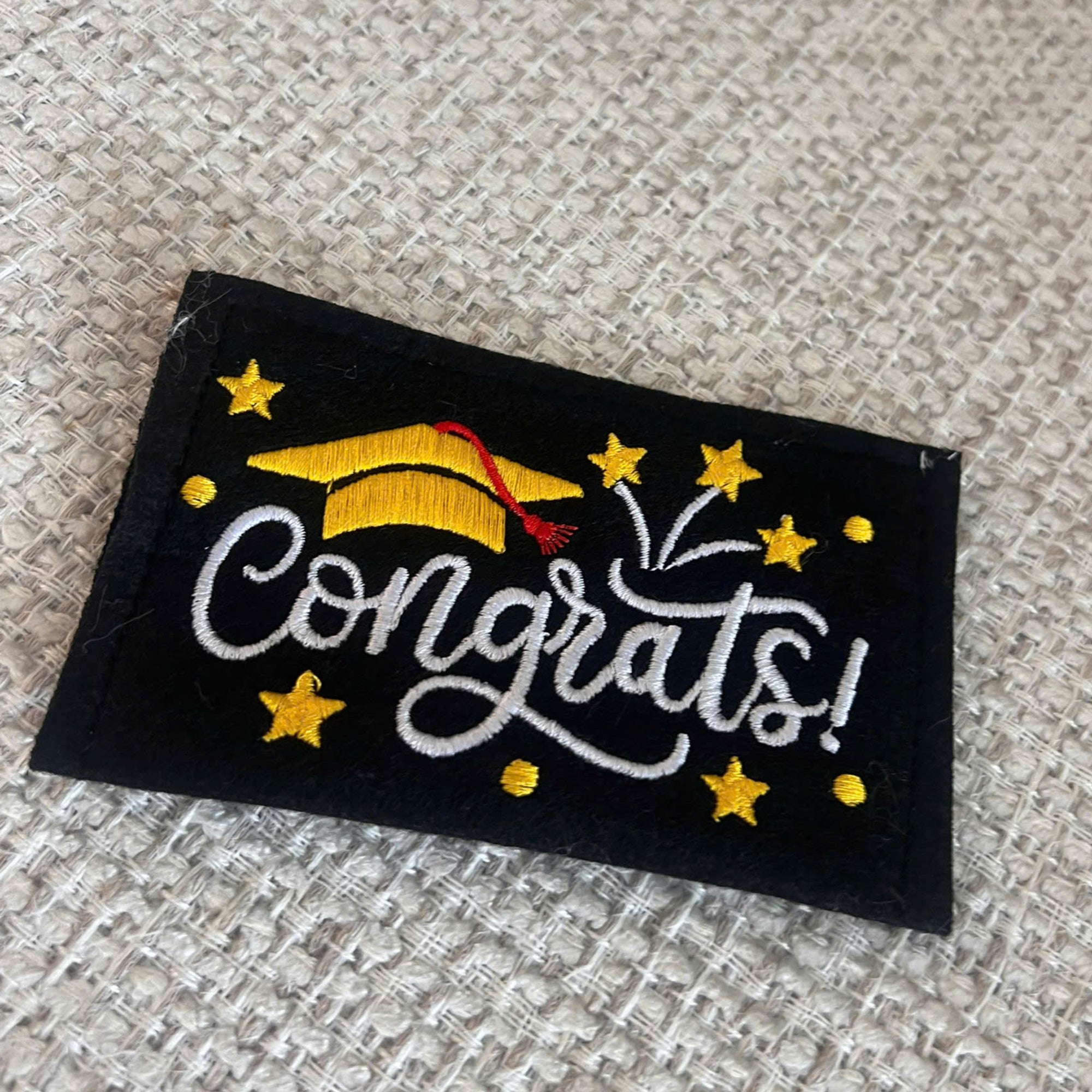 Embroidered patch with 'Congrats!' text and graduation cap design on a textured fabric background